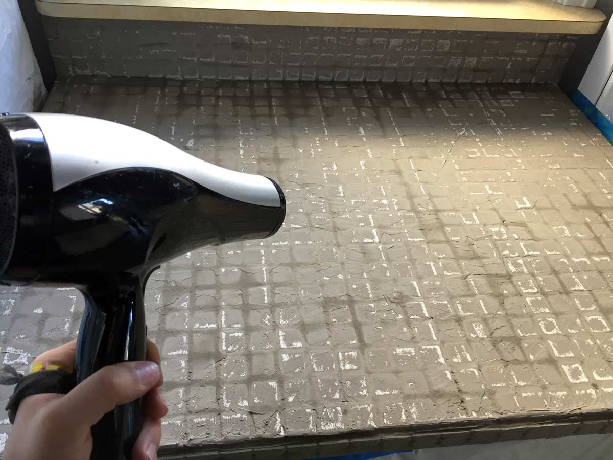 using a hair dryer to dry the first coat of feather finish concrete over tile counters